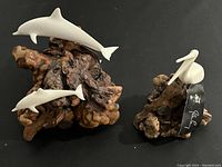 Photo showing both the dolphins sculpture and pelican sculpture on their respective burl wood bases with natural textures.