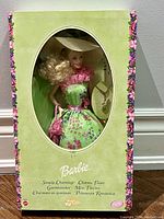 Front view of boxed Barbie doll in original packaging showing doll wearing green floral dress and hat, framed by pastel green box with floral border.