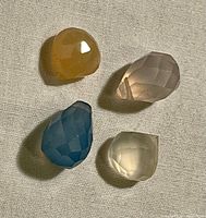 Four faceted quartz crystals including yellow, pale pink, blue, and white colours on a neutral fabric background.