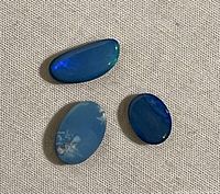 Three polished opals arranged on fabric background showing size and color variations.