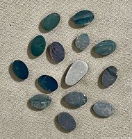 Image showing group of 15 assorted oval opal stones of various sizes and colours laid on beige fabric background.