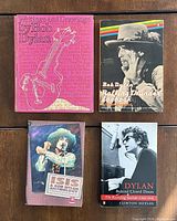 Four Bob Dylan books arranged on floor: 'Writings and Drawings by Bob Dylan,' 'Rolling Thunder Logbook,' 'Isis: A Bob Dylan Anthology,' and 'Dylan Behind Closed Doors'