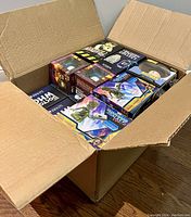 Open cardboard box filled with new collectible figures and toys in original packaging showing the top layer of items.