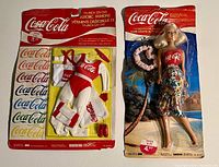 Two vintage Coca Cola collectible items in unopened, original packaging: a fashion doll and aerobic fashion clothing set with logos and accessories.