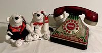 Photo showing two Coca Cola polar bear plush toys sitting next to a Coca Cola themed novelty telephone with a red handset.
