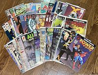 Full spread of 34 comic books fanned out on wooden floor showing various colorful titles and covers