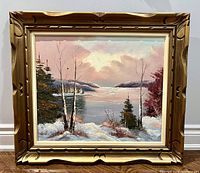 Front view of oil painting of a winter landscape with snow, trees by a lake and pastel sky, in a carved wooden frame.