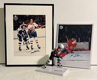 Framed and protected autographed hockey photos of Montreal Canadiens players on ice with one gloved collectible hockey figurine missing its stick in front.