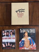 Top-down view of three books laid flat from the lot; one hardcover book titled 'Yesterday's Papers: The Rolling Stones In Print 1963-1984,' another hardcover book with Mick Jagger on the cover holding flags, and a softcover book titled 'Old Gods Almost Dead' by Stephen Davis.
