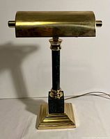Front view of the vintage bankers lamp showing the brass cylindrical shade and dark green marbled column on brass square stepped base.