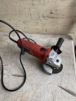 Red Skil angle grinder with power cord and side handle on a workbench