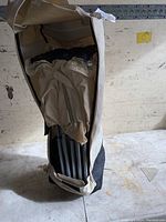 Foldable camping shelter packed in carrying bag showing metal frame and beige fabric canopy.