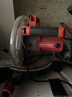 Close-up view of Craftsman radial arm saw showing the blade guard, handle with power button, and adjustable angle gauge on the base.