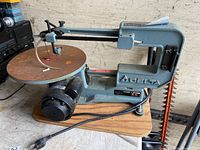 Front side view of the Delta 16 inch variable scroll saw showing the blade, motor, and wooden base.