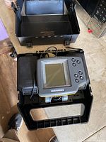 Open black plastic carrying case containing Humminbird V702 fish finder device with screen and control buttons.