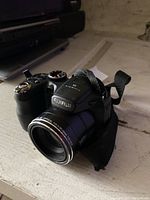 Photo of a black Fujifilm FinePix digital camera with 12x optical zoom lens on a white surface.