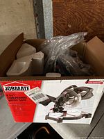 Opened cardboard box containing the Jobmate 8 1/4 compound mitre saw, secured with styrofoam and plastic packaging, showing the product box with details.