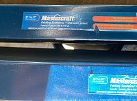 Close-up photo of the Mastercraft label showing size, capacity 300 lb, non-slip padded surface, and pre-drilled holes for tabletop installation.