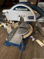 Photo showing the Mastercraft mitre saw with circular blade, angle adjustment scale, and laser guide on a wooden surface.