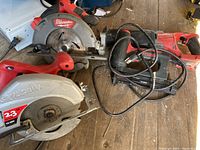 Four assorted power tools laid on wooden floor: Milwaukee and Skilsaw circular saws, Milwaukee brad nailer, Craftsman electric drill