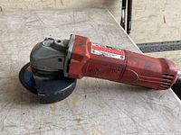 Angle grinder placed on a scratched work surface, showing side profile with Milwaukee logo and grinding disc.