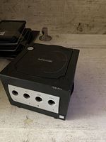 Black Nintendo GameCube console with visible controller ports and memory card slots on front, top loading disk drive, and some surface wear.