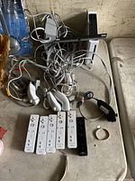 Top-down view showing six Nintendo Wii wireless controllers (five white, one black) with six white Nunchucks and various cables on table.