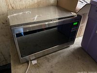 Front and side view of the Panasonic stainless steel microwave with the digital display illuminated, showing the appliance's exterior and control panel.