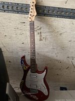 Full front view of red Peavey electric guitar showing body with stickers, pickguard, pickups, and neck against a metal and worn background.