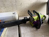 Poulan chainsaw placed on table showing full side view of chainsaw with blade cover attached. Chainsaw body is green and purple with black handles.