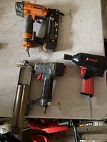 Photo showing two pneumatic nailers and one pneumatic impact wrench on a white surface.