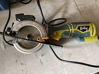 Photo of Radley compact circular saw showing blade, blade guard, handle and power cord on a floor surface.
