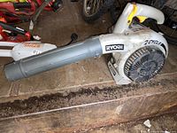 Side view of Ryobi 2 cycle gas powered handheld leaf blower on wooden surface.