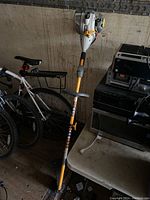 Full view of the Ryobi gas powered trimmer leaning against a wall next to a bicycle and other items.