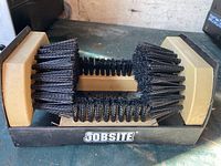 Photo of Jobsite shoe cleaning brush showing three sides with dense black bristles attached to a beige plastic body and mounted on a black base.