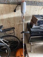 Full view of Stihl electric grass trimmer leaning against a wall with a bicycle nearby, showing overall length and components