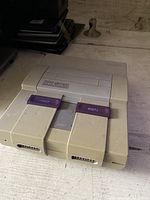 Photo showing a close-up angled view of a Super Nintendo Entertainment System (SNES) console on a surface, capturing power and reset buttons, cartridge slot, and front controller ports.