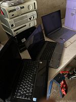 Three laptops on a workbench with stacked electronics in background