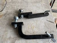 Photo showing two trailer hitches with attached balls lying on a gray surface.