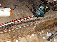 Green and yellow electric hedge trimmer with long blade placed on wooden bench.