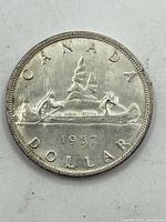 Reverse side of 1957 Canadian silver dollar coin showing two men paddling a canoe and 'CANADA DOLLAR 1957' inscription.