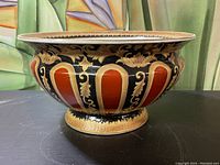 Front side of ceramic planter showing ornate orange, gold, and black pattern with pedestal base