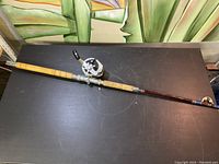 Full view of the fishing rod with attached Ryobi Adventure reel on a black surface.