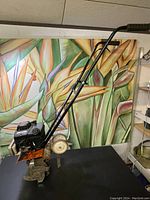 Full rototiller showing black gas engine, orange base plate with CT16 model marking, metal tines with residual soil, white wheels, and black handlebars.