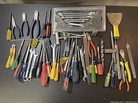 Overview of assorted hand tools including pliers, wrenches, screwdrivers, putty knife, and clamp on a black background.