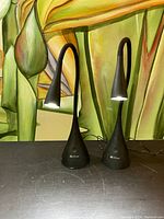 Front view of both black OttLite LED table lamps with lights on, showing their flexible necks and cone bases.