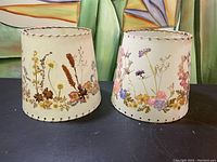 Front view of two vintage floral lampshades placed side by side showing detailed flower patterns and stitched edges.