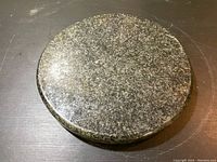 Top and side view of round granite cutting board showing its thickness and speckled granite surface.