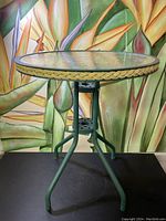 Front view of small vintage patio table with green metal frame and braided trim around glass top