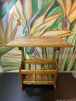 Front view of the solid oak side table showing the rectangular top and storage rack with vertical slats underneath, set against a colorful floral background.
